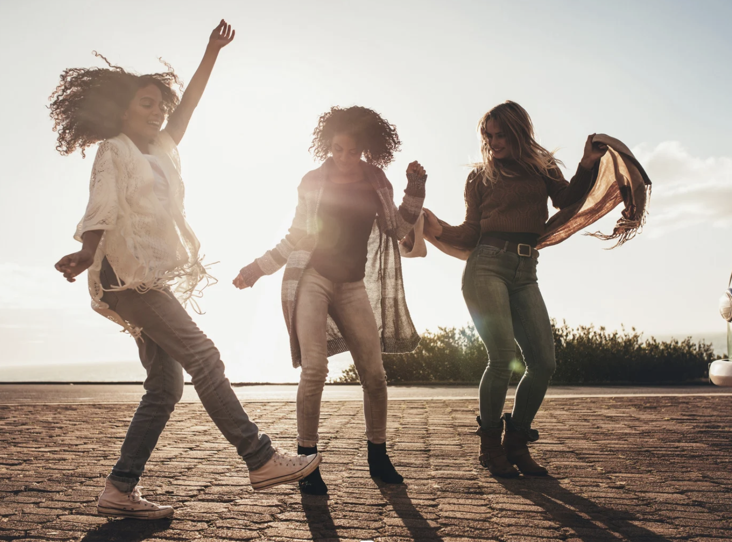 Three women dancing together outside.